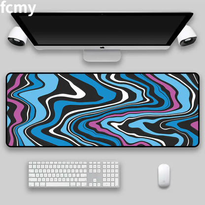 A desktop setup featuring a large monitor, two speakers, and a keyboard accompanied by HomeForDecor's Art Strata Liquid Mouse Pad. This durable fabric desk mat can also serve as a mouse pad and is adorned with an abstract wavy pattern in black, white, blue, and purple created through the sublimation process.