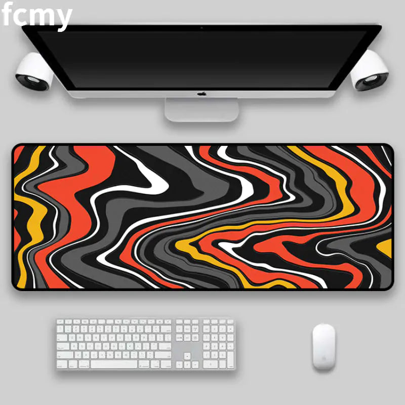 A computer setup that includes a sleek monitor, keyboard, and mouse, complemented by the HomeForDecor Art Strata Liquid Mouse Pad. This mouse pad features vibrant colors in red, black, white, and yellow with an abstract wavy pattern. Its durable fabric enhances the minimalist workspace with a pop of color.