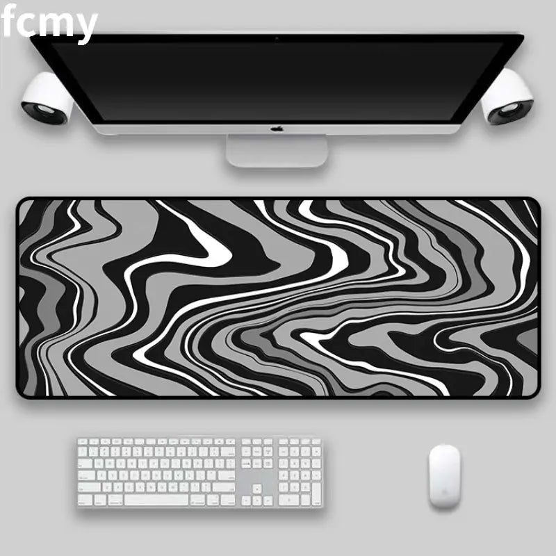 Under an Apple keyboard, mouse, monitor, and speakers on a gray desk lays the Art Strata Liquid Mouse Pad by HomeForDecor, featuring a sleek grayscale abstract wavy design. It is expertly crafted with durable fabric through the sublimation process.